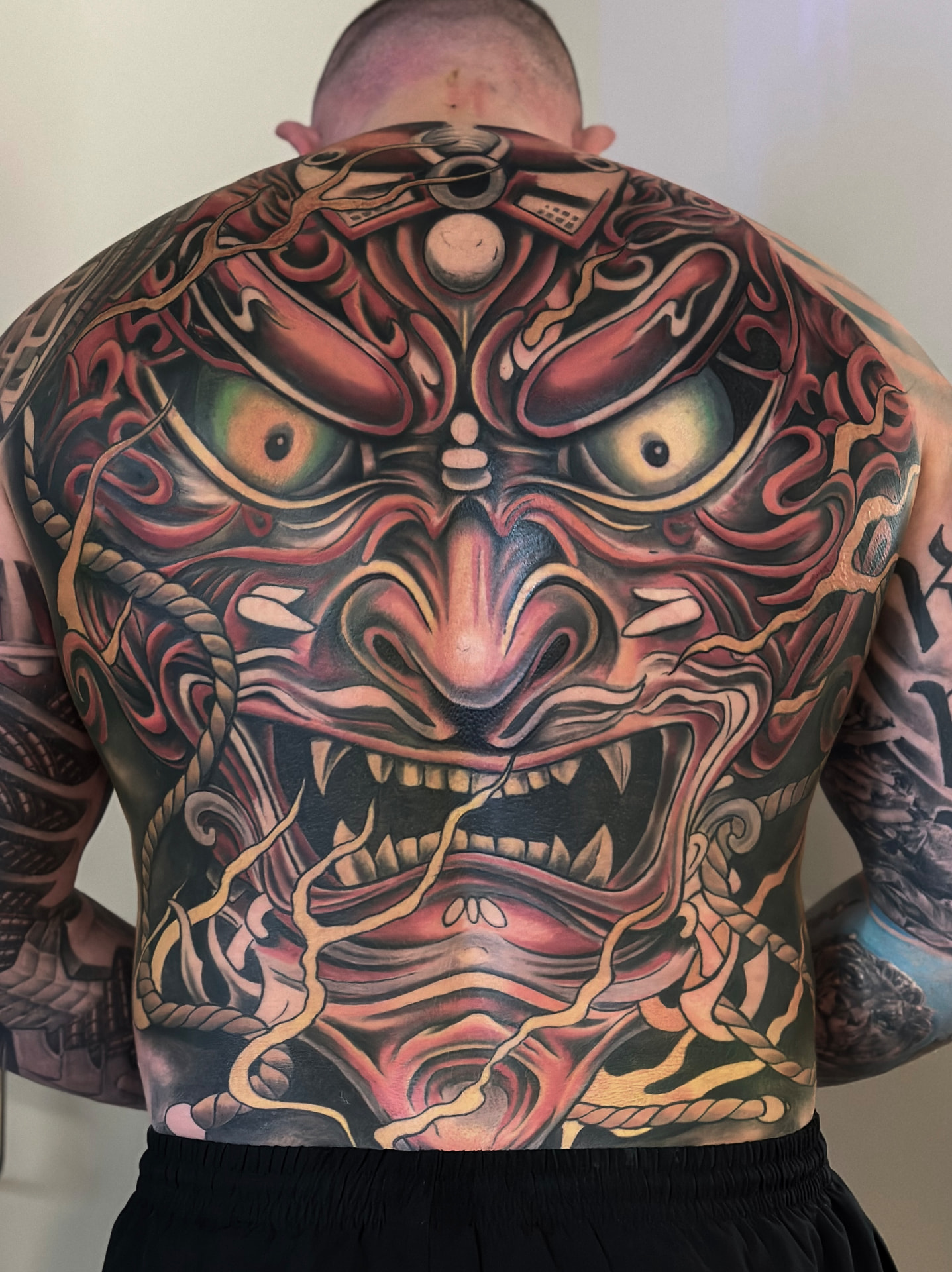 Farvet rygtatovering med stor japansk hannya- og oni-maske i røde og gule toner
