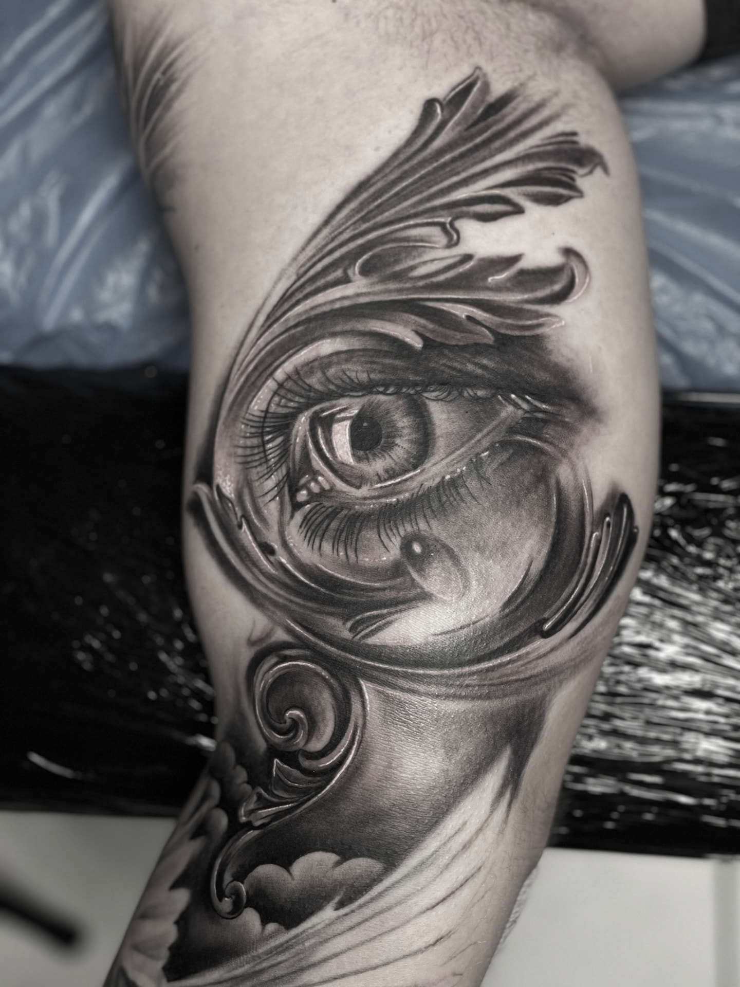 Black and grey tatovering af realistisk øje med barokke ornamenter på overarm