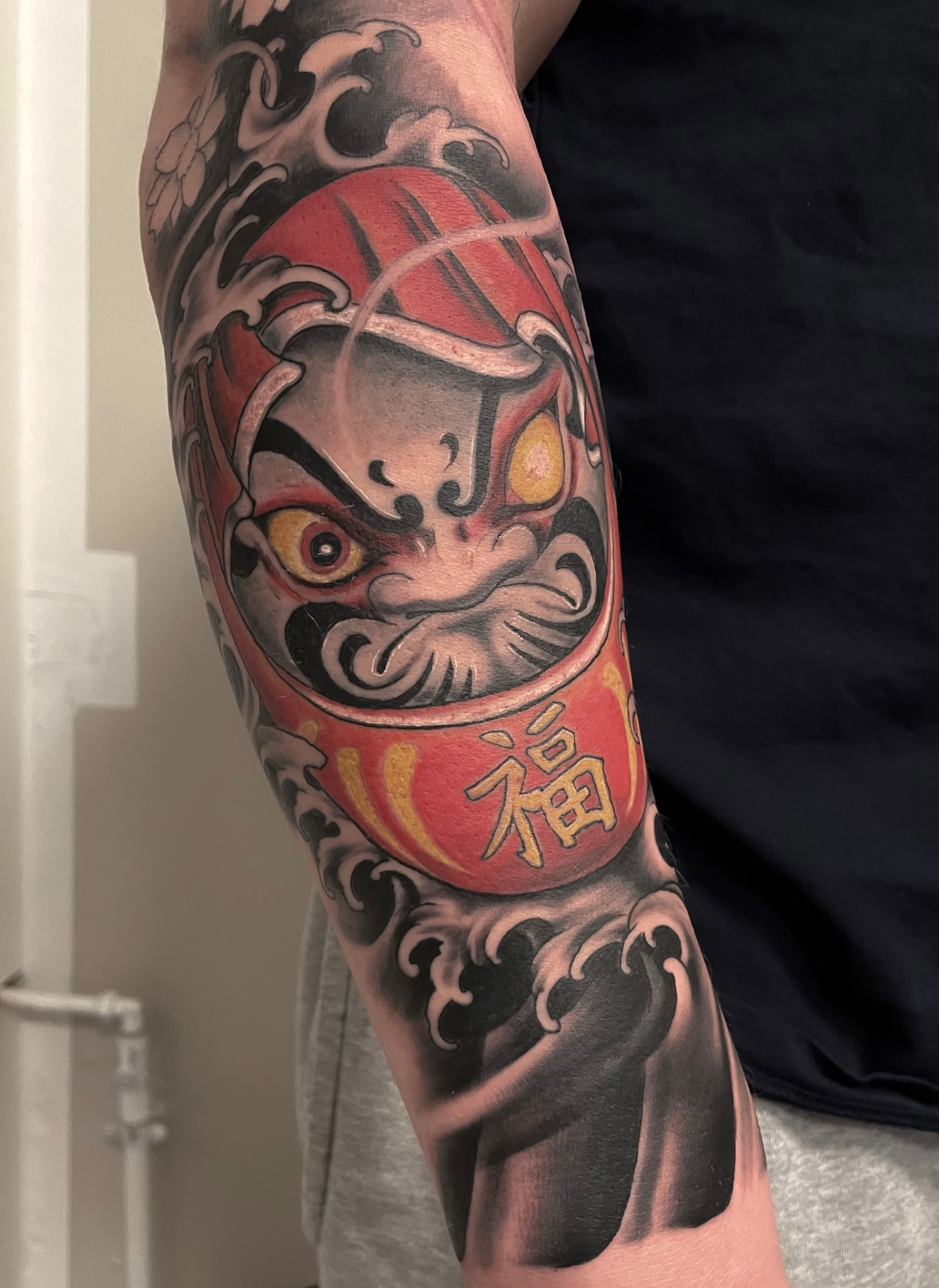 Japansk farvetatovering af rød daruma-dukke med bølger på arm