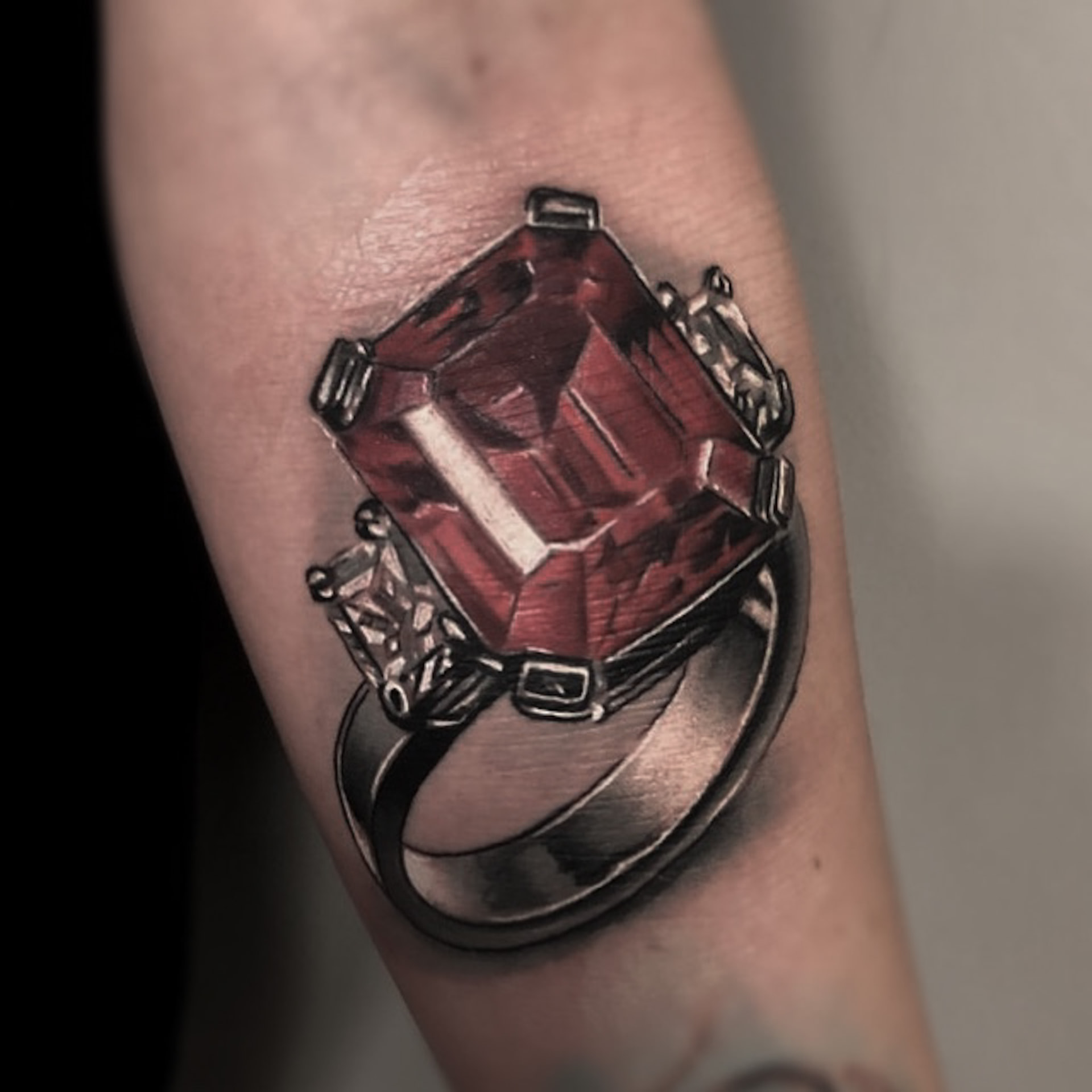 Realistisk farvetatovering af ring med rød sten og diamanter på underarm