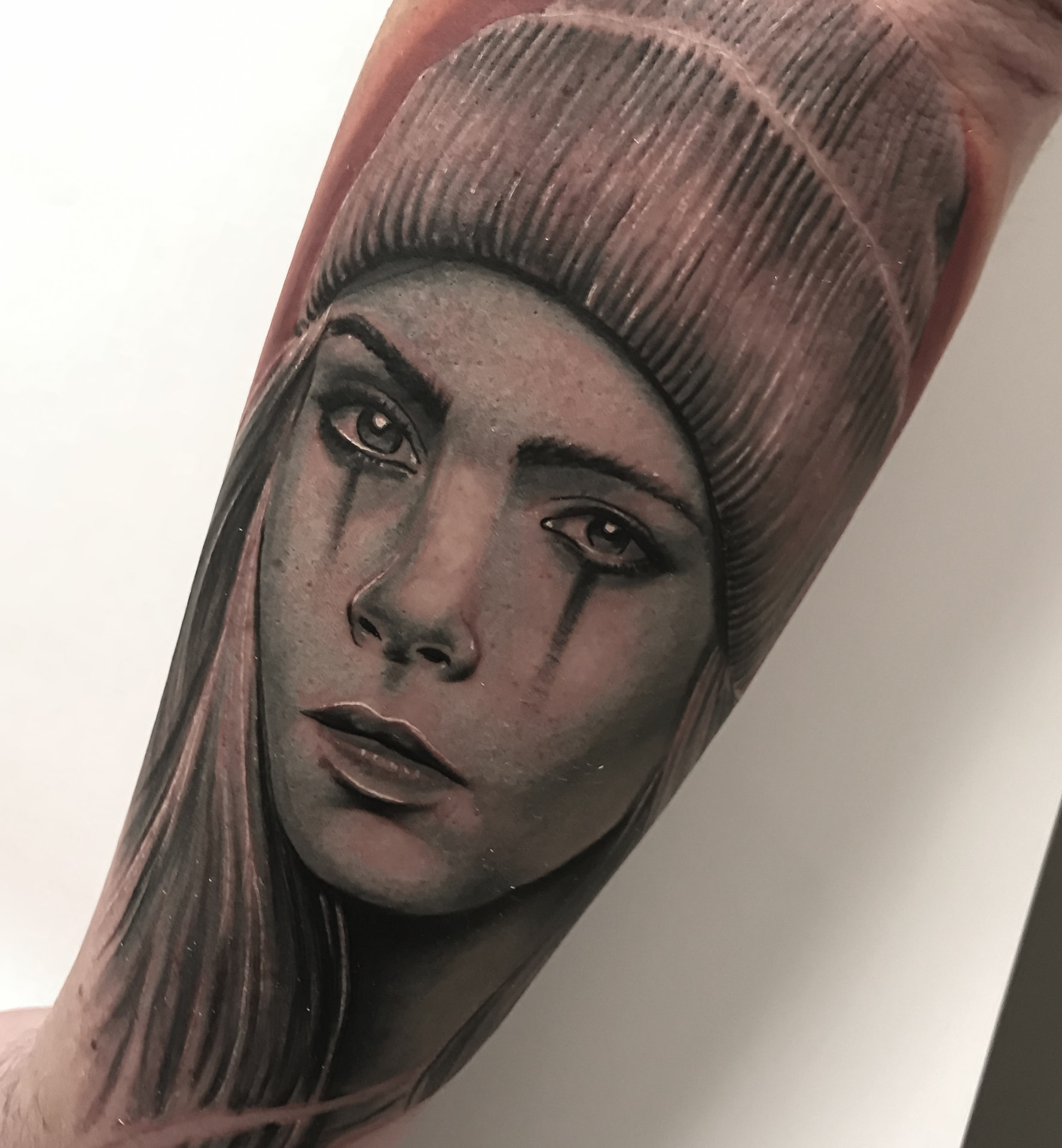 Black and grey portrættatovering af kvinde med hue og sorte tårer på underarm