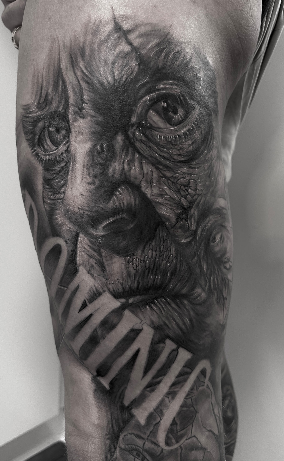 Black and grey horror-tatovering med forvredet ansigt og lettering på arm