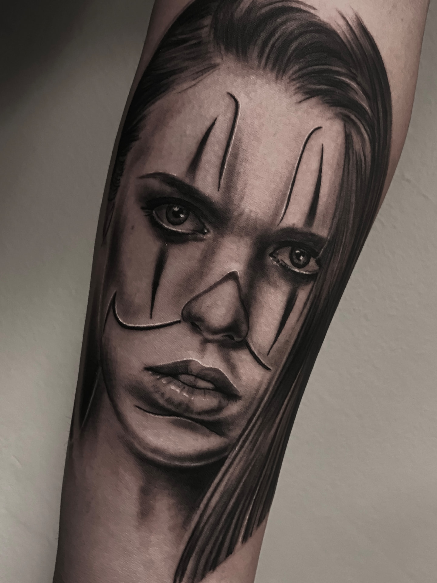 Black and grey portrættatovering af kvinde med klovnemakeup på underarm