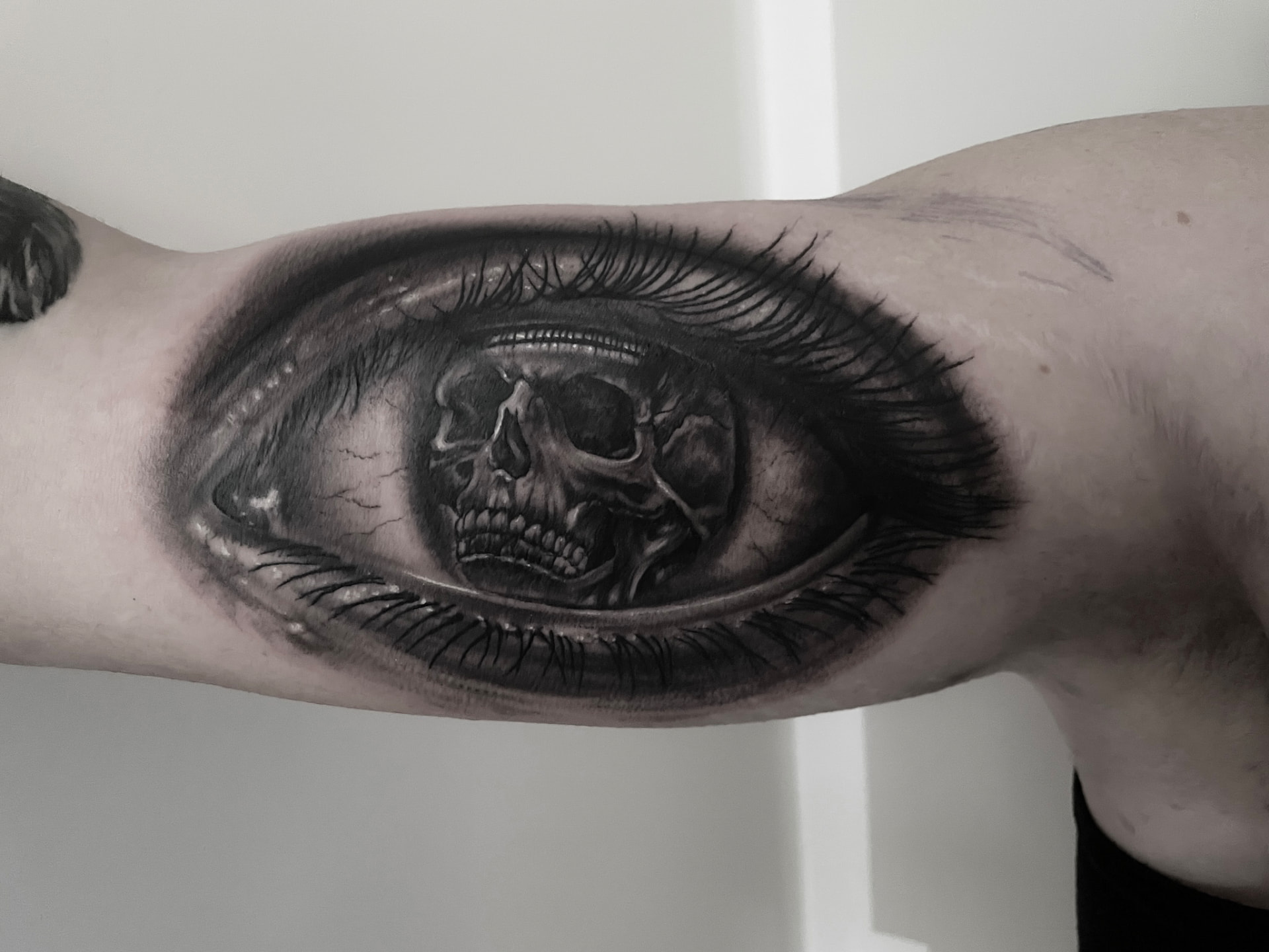 Realistisk black and grey tatovering af øje med kranie i pupillen på overarm