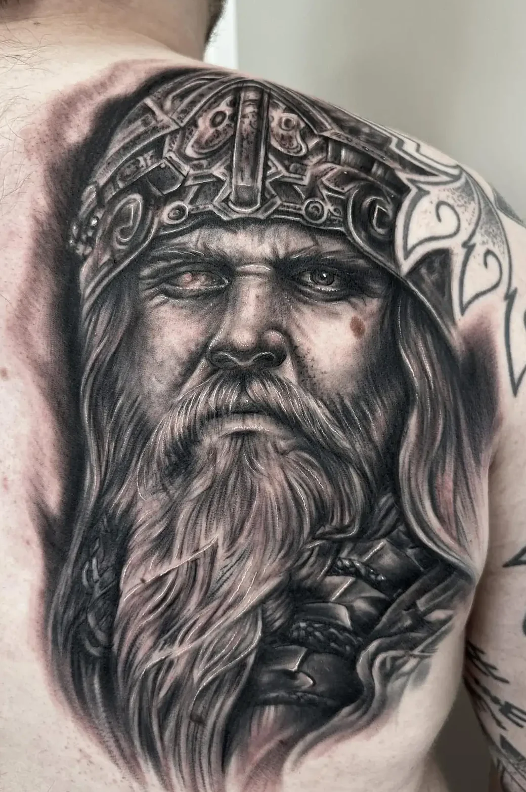 Black and grey tatovering af nordisk kriger med hjelm og skæg på skulder