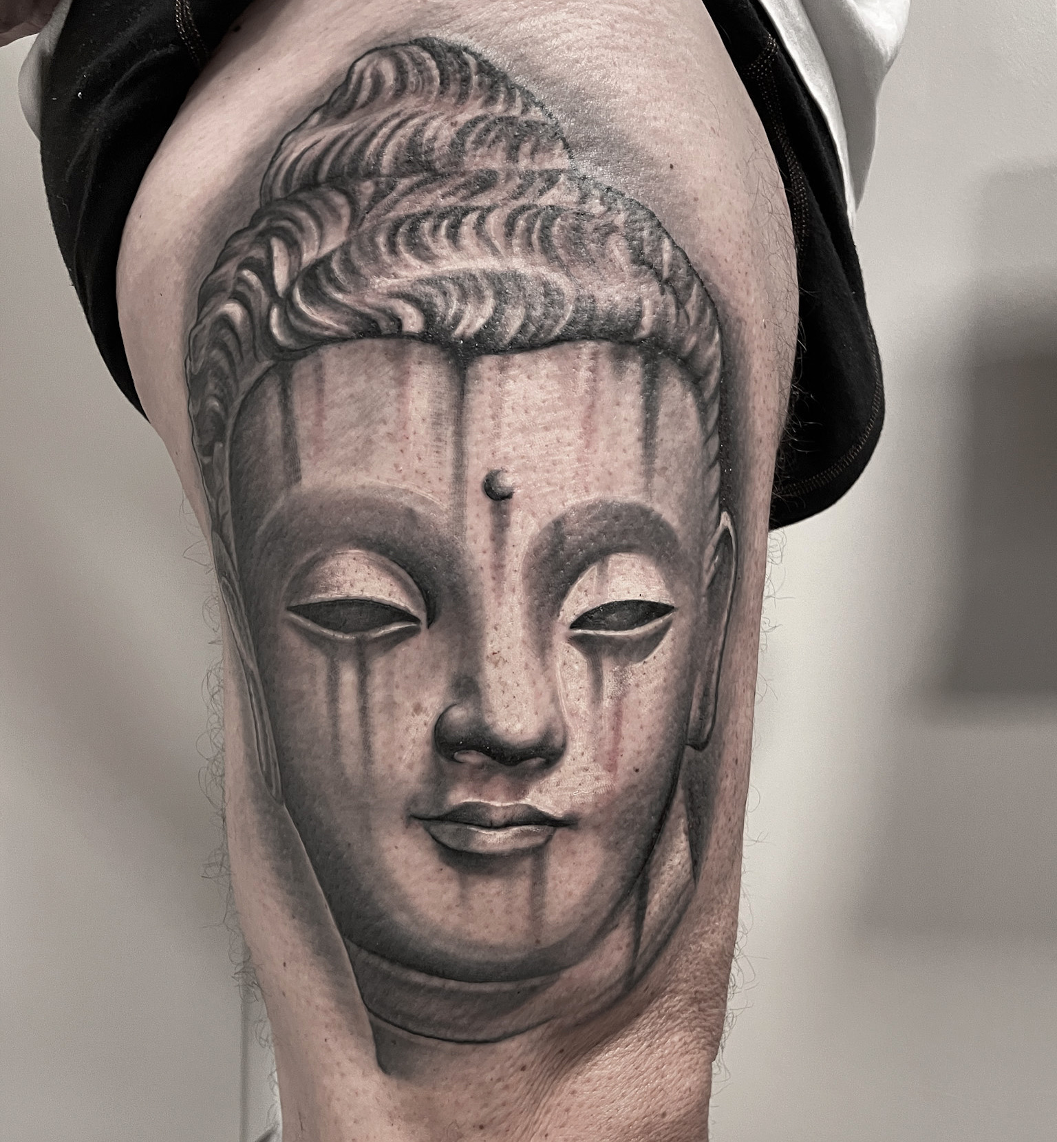 Black and grey tatovering af buddhastatue i sten på overarm