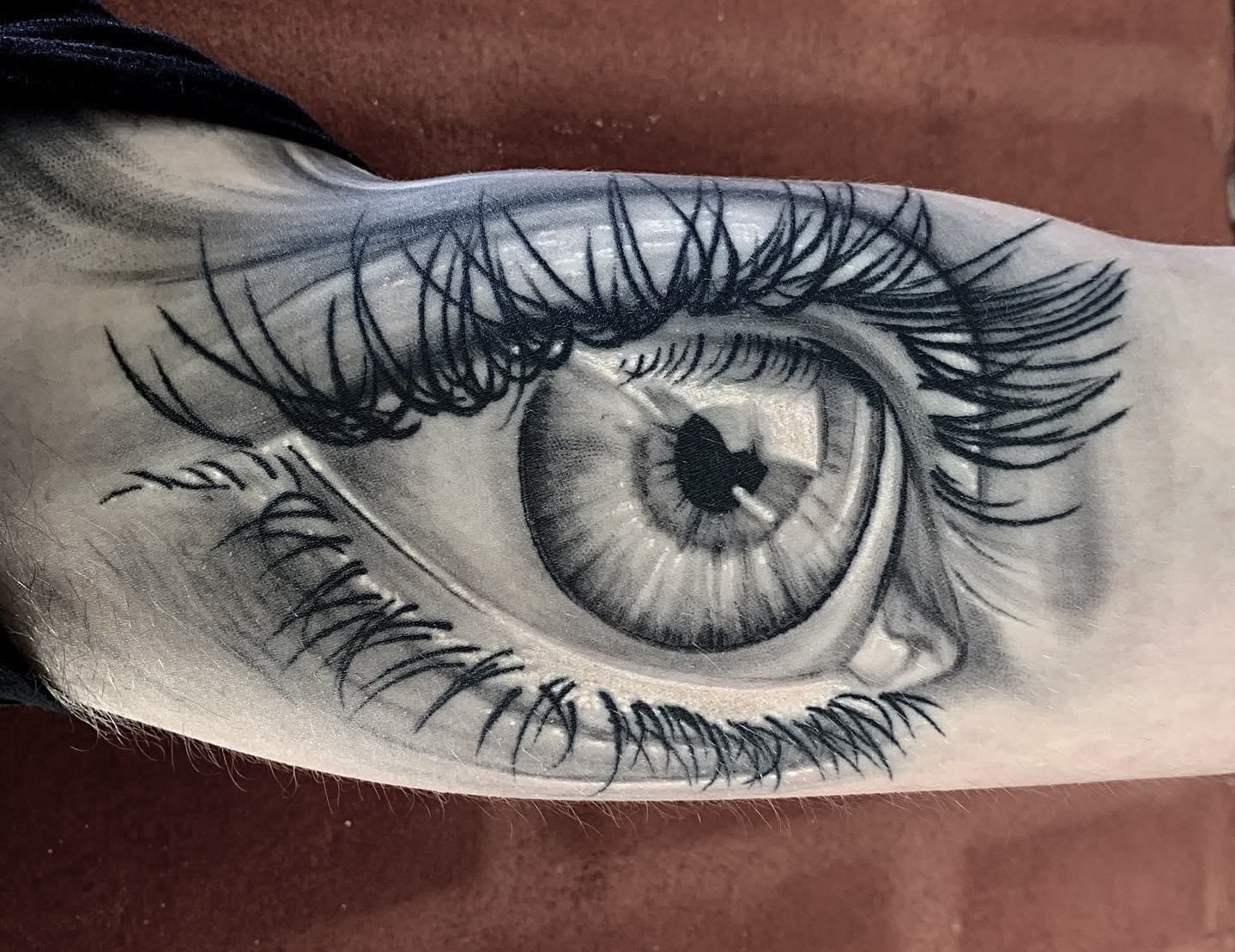 Realistisk black and grey tatovering af stort øje med lange øjenvipper på underarm