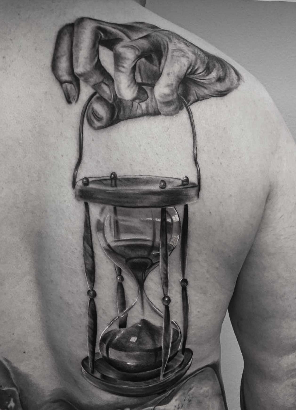 Black and grey rygtatovering med hånd der holder et realistisk timeglas