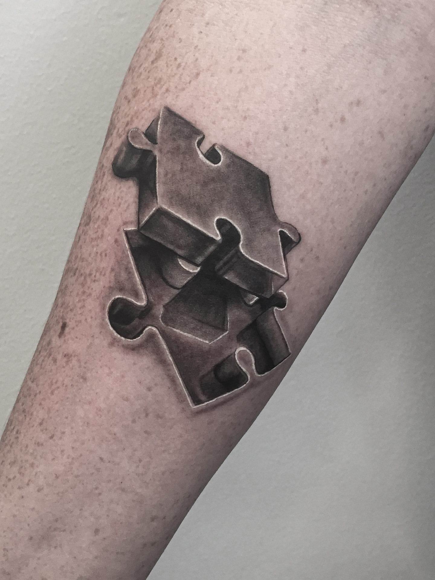 Black and grey tatovering af puslespilsbrikker med 3D-effekt på underarm