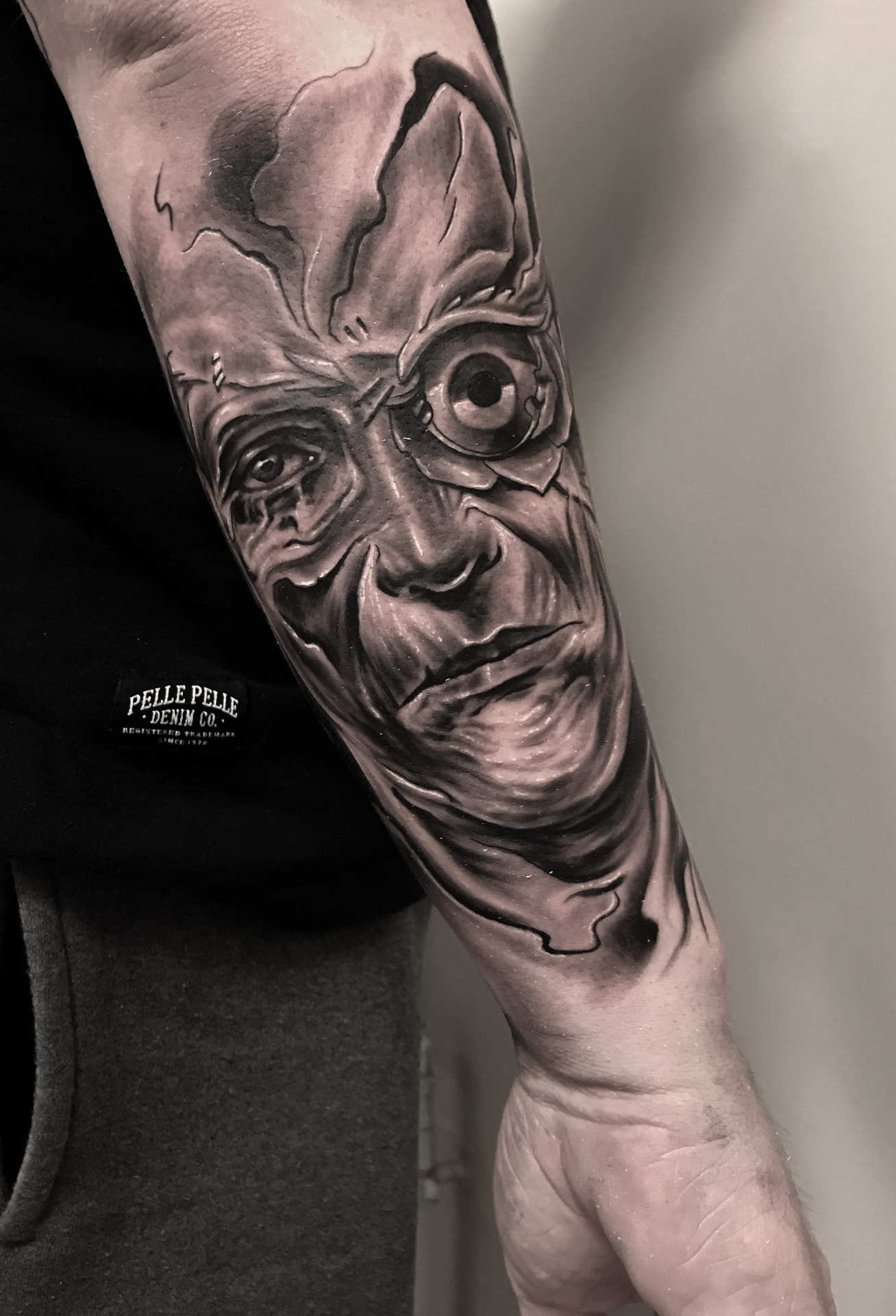 Black and grey horror-tatovering af uhyggeligt ansigt med stort øje på underarm