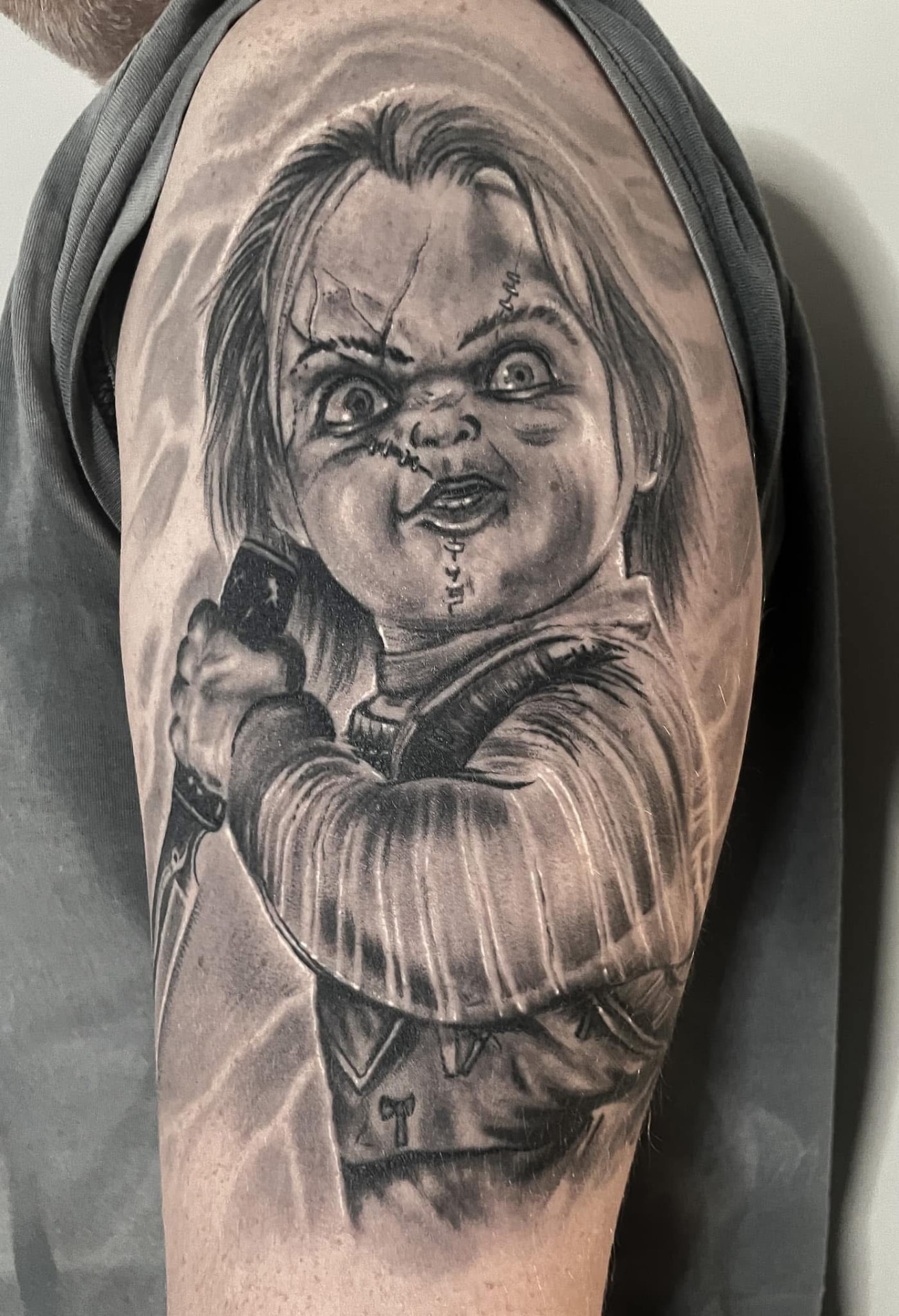 Black and grey portræt af Chucky-dukken med kniv på overarm