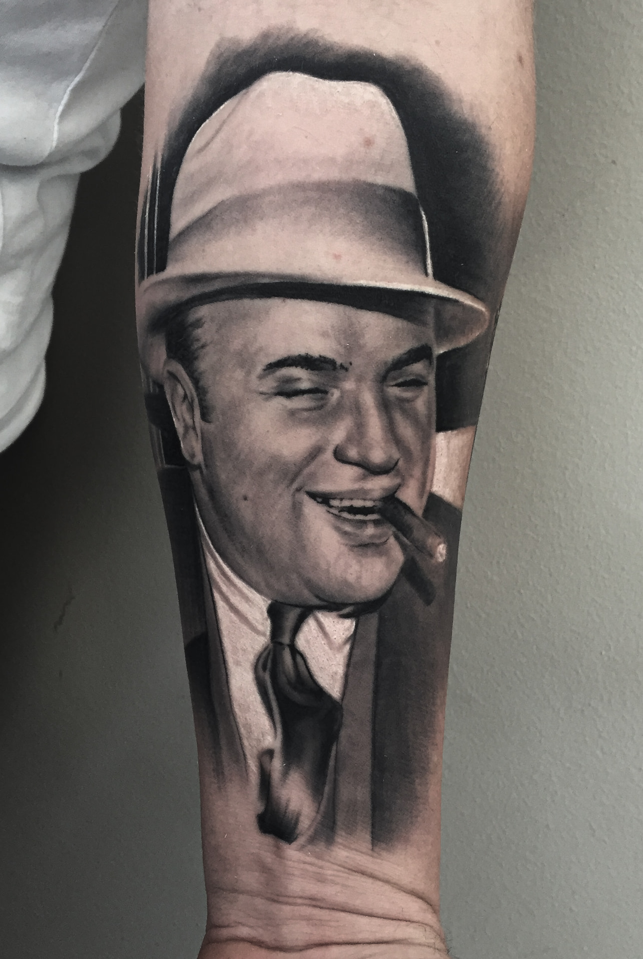 Black and grey portrættatovering af gangster med hat og cigar på underarm