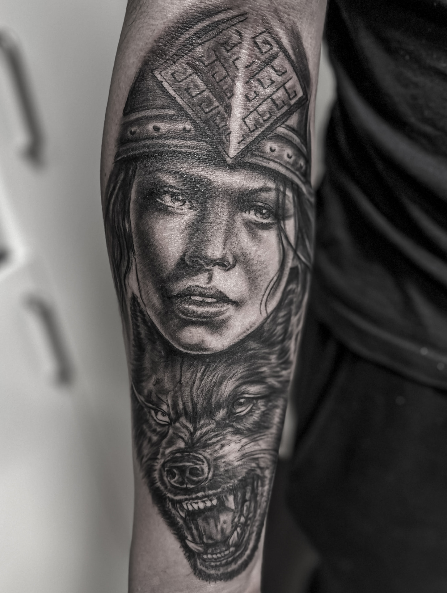 Black and grey tatovering af krigerkvinde med hjelm og ulv på underarm