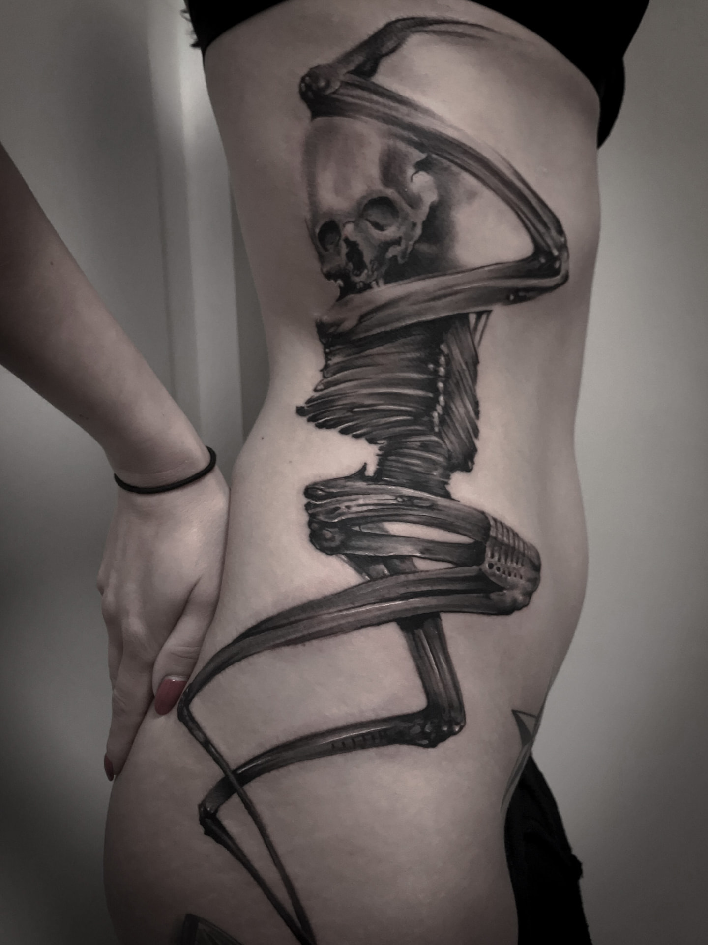 Black and grey tatovering af realistisk skelet der snor sig om hofte og ribben