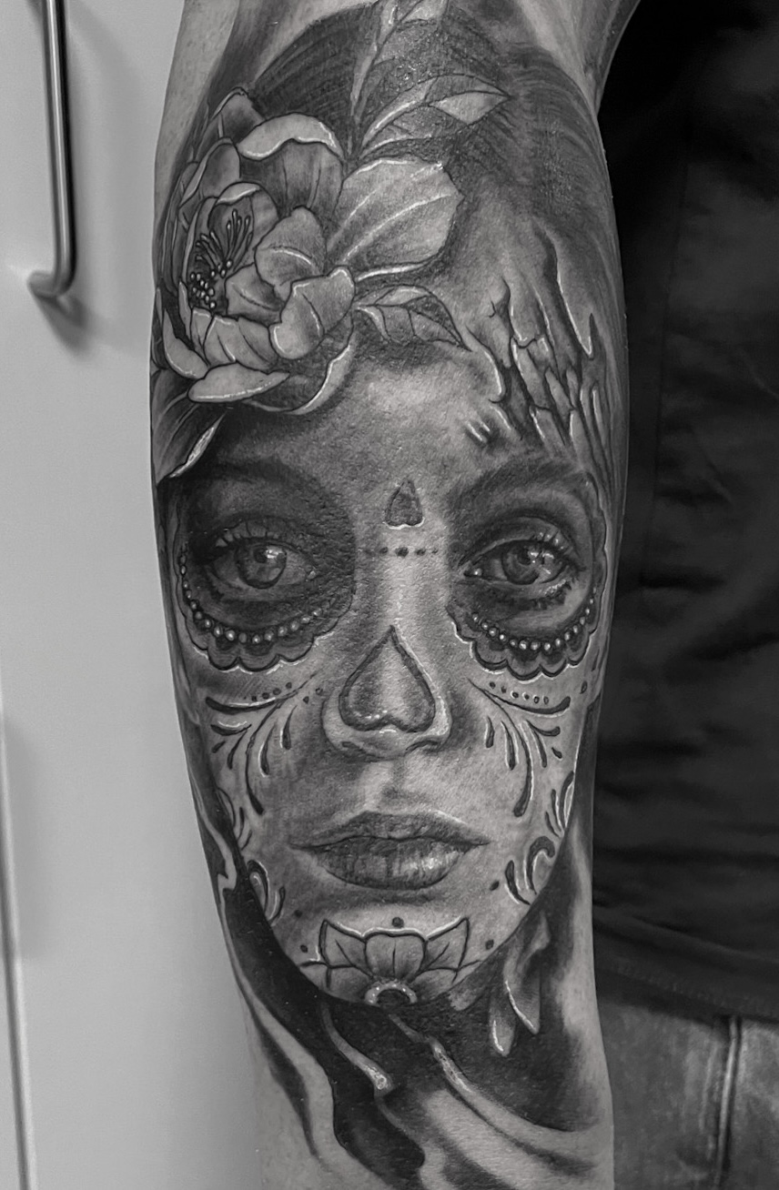 Black and grey catrina-tatovering af kvinde med sugar skull-makeup og blomst på underarm