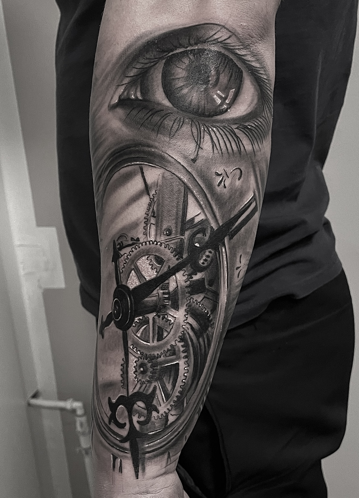 Black and grey tatovering af realistisk øje over urværk med tandhjul på underarm