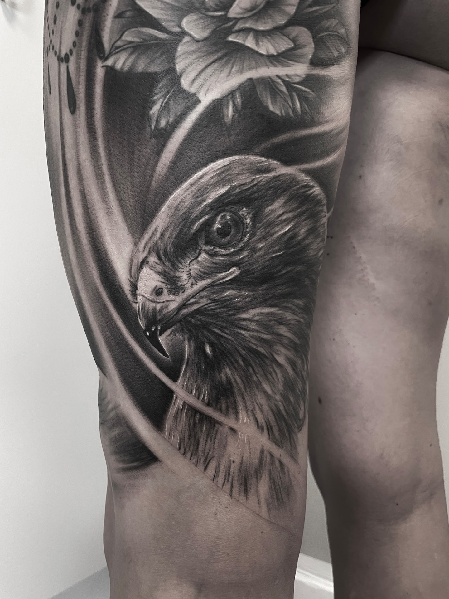 Black and grey tatovering af ørnehoved med rose og draperi på lår