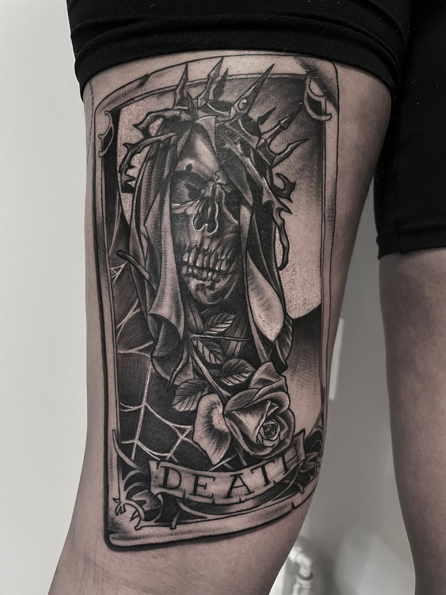 Black and grey tarotkort-tatovering med Death, kranie i kappe og rose på lår