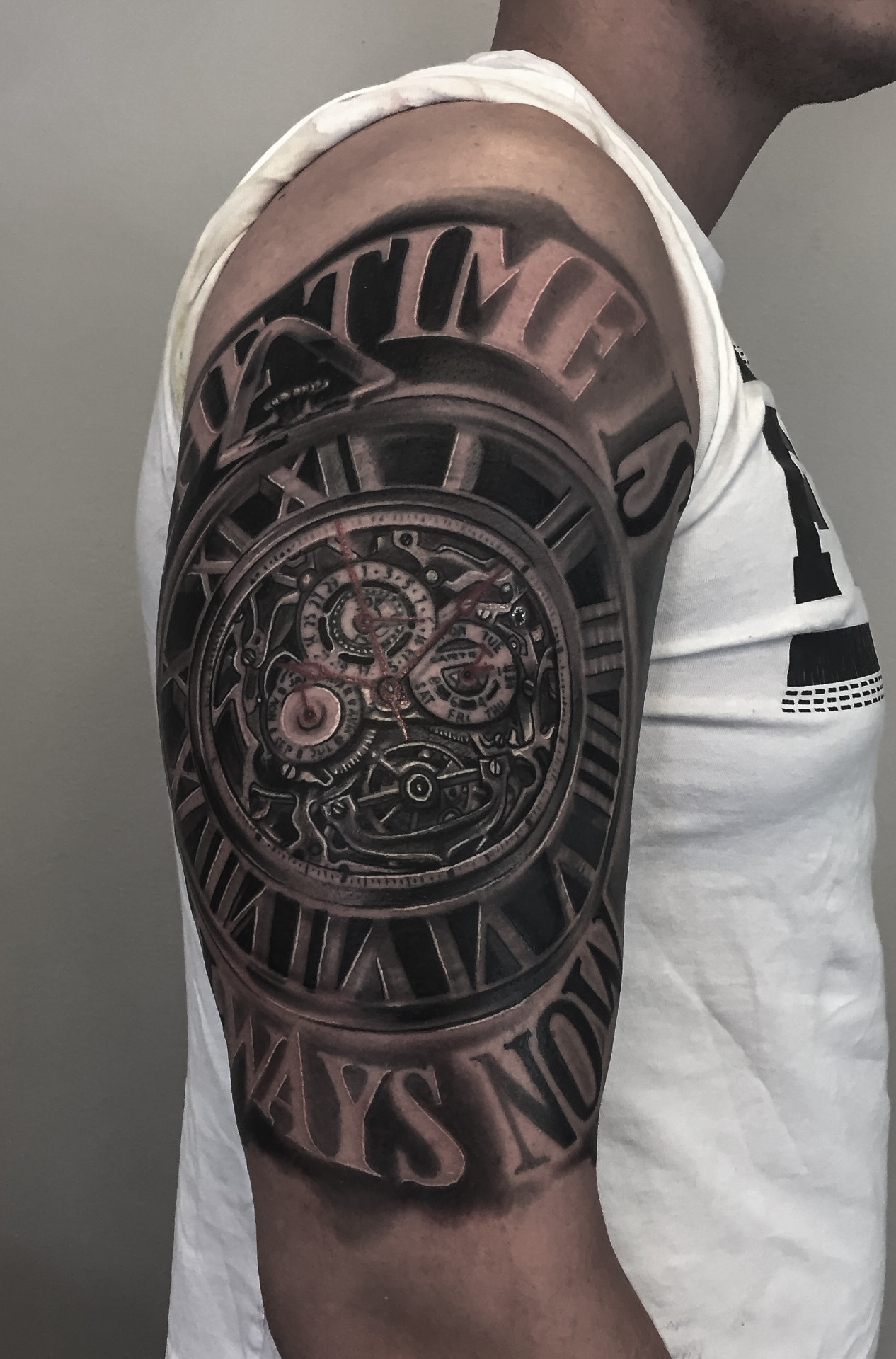 Black and grey tatovering af lommeur med urværk og teksten Time is always now på overarm