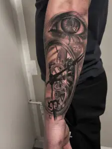 Realistisk tatovering af øje og urværk på underarm – black & grey tattoo med symbolik og mekaniske detaljer
