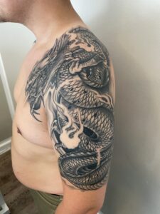 Japansk-inspireret drage-tatovering i sort og grå, der dækker bryst og overarm