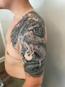 Japansk-inspireret drage-tatovering i sort og grå, der dækker bryst og overarm, lavet af Tattoo Mini