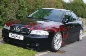 Full view of a custom black sedan with hyperrealistic red and orange flames airbrushed across the hood and sides, lowered suspension and polished alloy wheels.