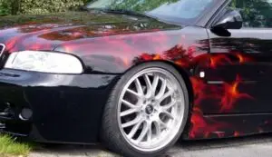 Custom-painted car with hyperrealistic red and orange flames airbrushed over the front fender and side, paired with polished silver racing rims.