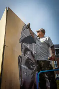 Kunstner i gang med stort vægmaleri med spraydåse