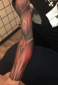 Full forearm tattoo depicting exposed muscle fibers in red and black tones, stylized to resemble peeled-back skin with artistic flow and anatomical realism.