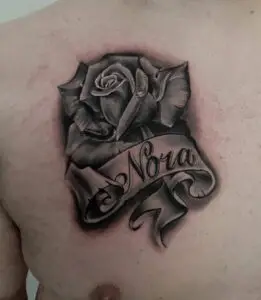 Black and grey tattoo of a rose with a flowing banner featuring the name “Nora”.