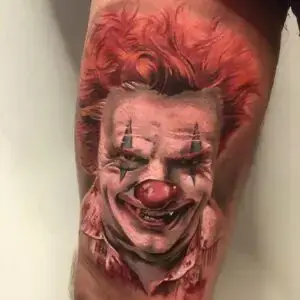 color tattoo of a sinister clown with bright red hair, smeared makeup, and a menacing smile.