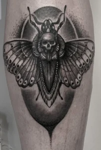 Black and grey tattoo of a death’s-head moth with skull and ornamental detailing.