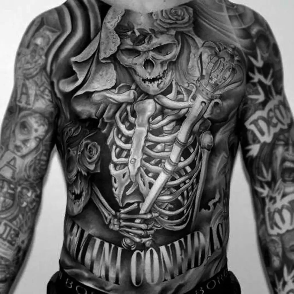 Full torso black & grey tattoo of a skeleton with crown and scepter, surrounded by roses, skulls, and the words “REMINI CONFIDAS”. Trust no one
