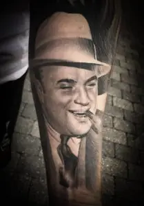 Realistisk tatovering af Al Capone i jakkesæt og hat med cigar i munden.udført af Tattoo Mini