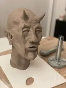 Realistisk skulptur af dæmonisk mand med horn og spidse ører i ler