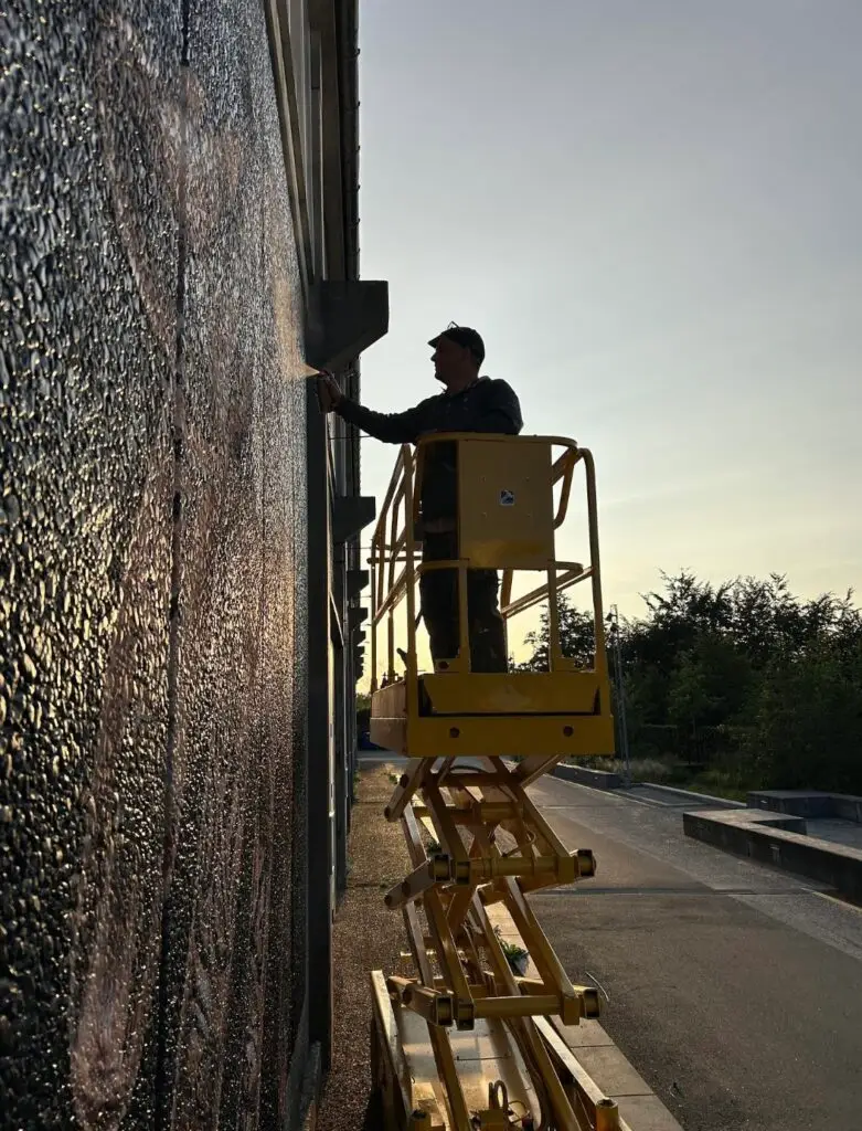 Streetart-kunstner sprayer vægmaleri fra lift i solnedgang