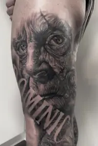 Tatovering af ældet ansigt med dramatiske detaljer og teksten “DOMINIC”