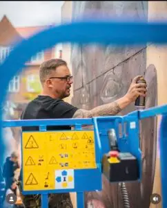 Tatovør og kunstner maler væg med spraydåse fra lift