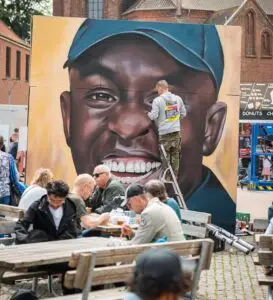 Streetart kunstner maler stort portræt foran publikum på torv