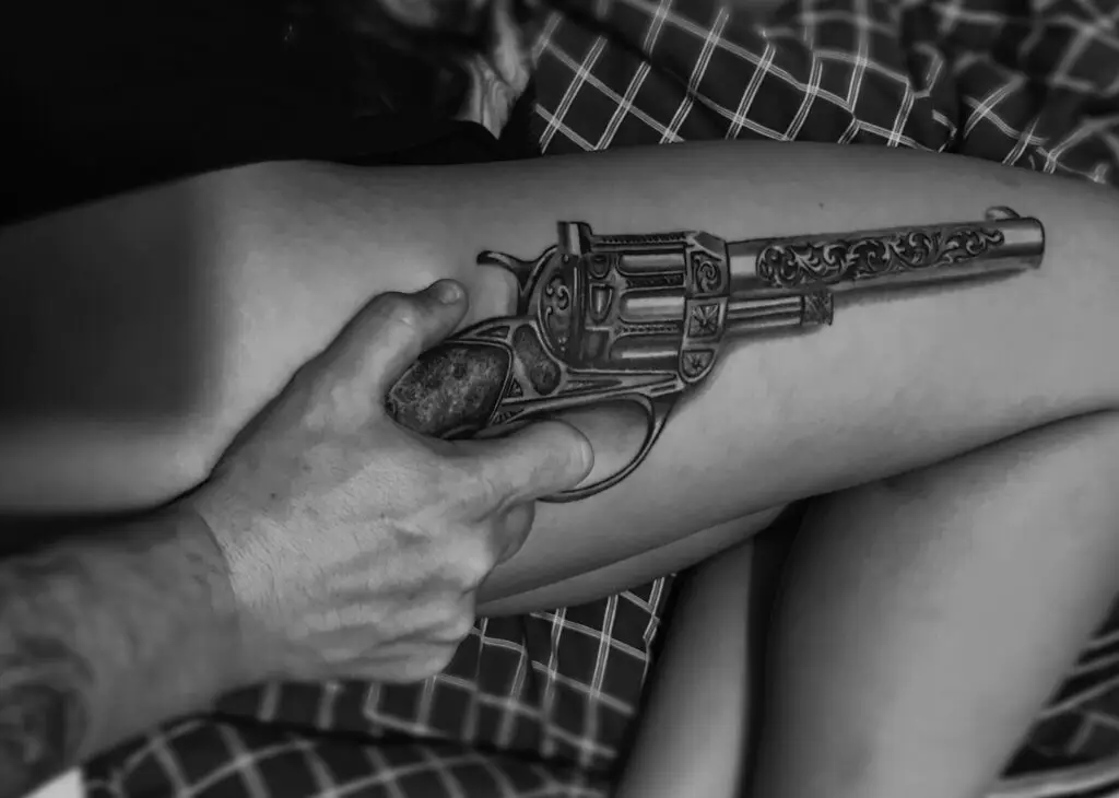 Tatovering af revolver på lår, holdt realistisk med hånd af Tattoo Mini