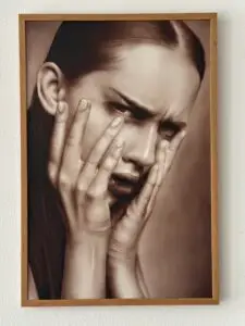 Sepia toned airbrush portrait of a distressed woman pressing her face with both hands
