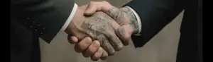 Håndtryk mellem tatovør med tatoveret hånd og kunde i jakkesæt. Symbol på tillid og samarbejde