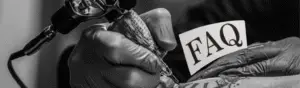 atovør med sorte handsker, der holder en tatoveringsmaskine og et kort med teksten FAQ.