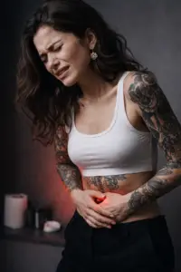 Kvinde med tatoveringer der oplever menstruationssmerter og holder sig om maven før tatovering. Tattoo & menstruation Fra Tattoo Mini
