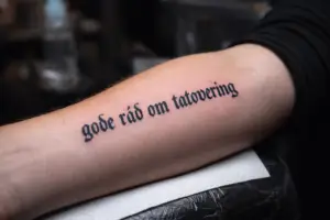 Arm med frisk tatovering med teksten “gode råd om tatovering” – professionelt udført sort tekst-tatovering.Fra Tattoo Mini