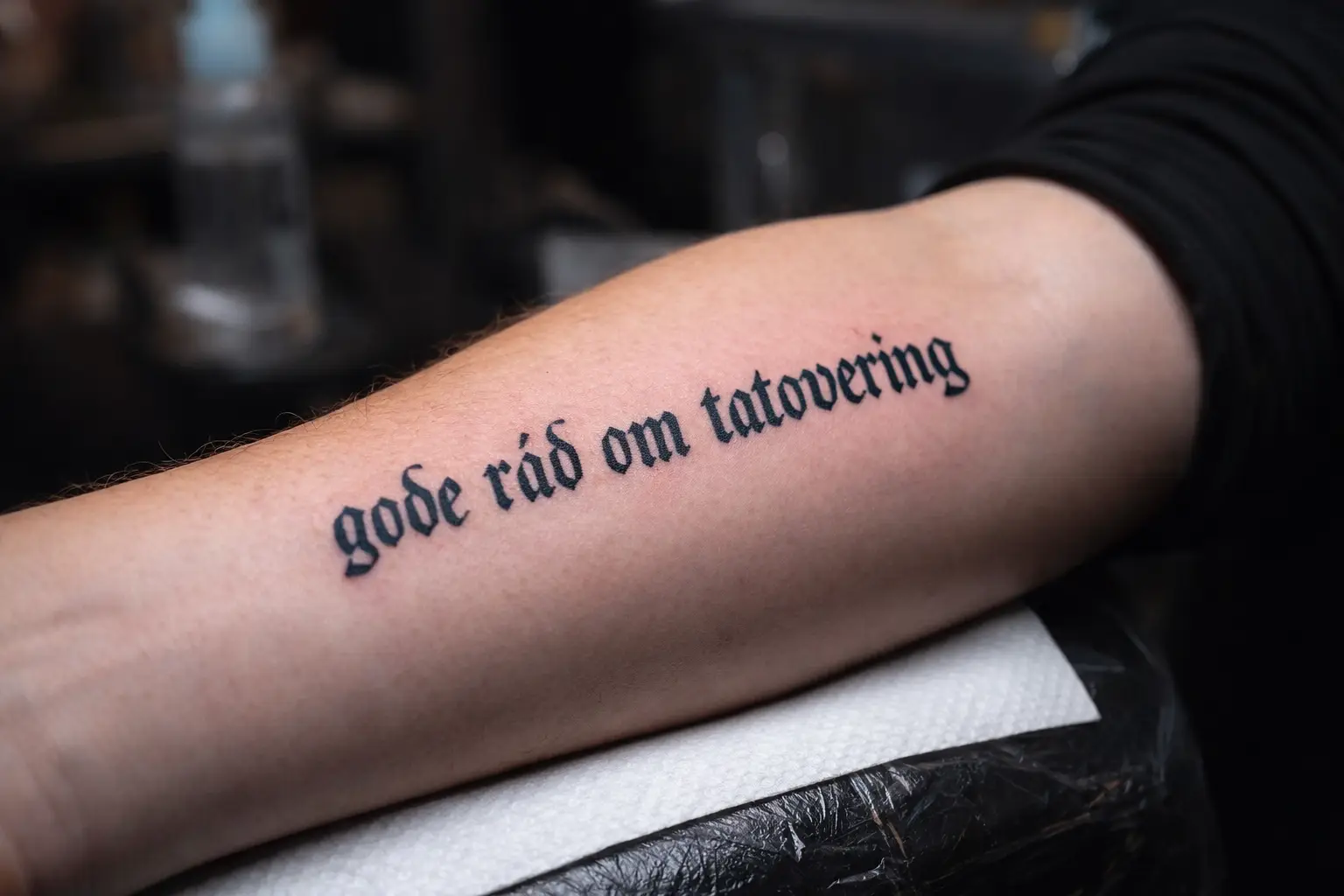 Arm med frisk tatovering med teksten “gode råd om tatovering” – professionelt udført sort tekst-tatovering.Fra Tattoo Mini