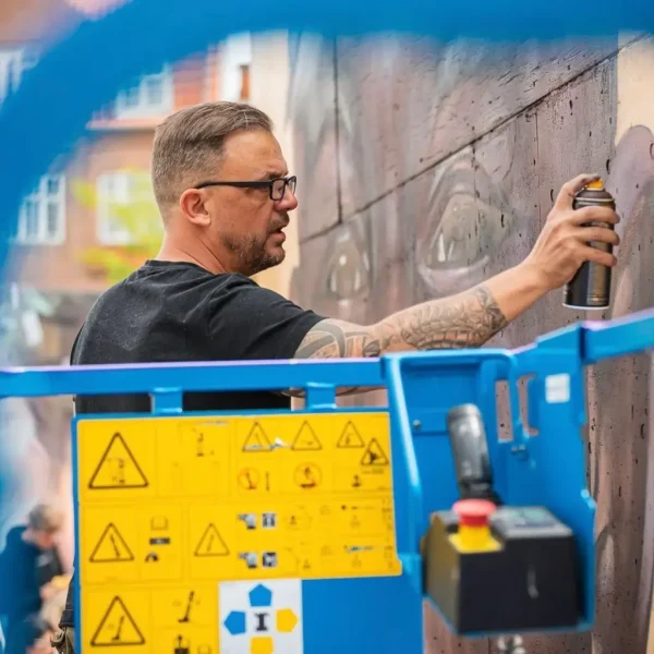 Tatovør og street art-kunstner maler væg med spraymaling fra lift i bymiljø.slagelse lift.